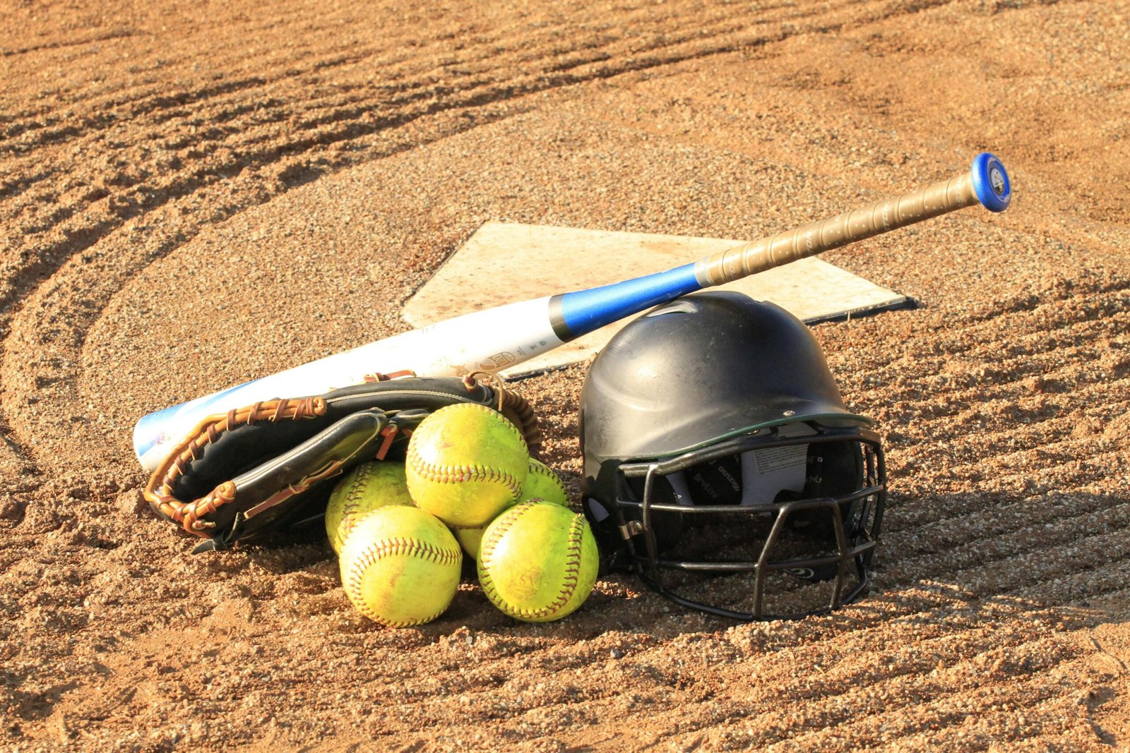 Close-up of baseball and softball gear on a dirt field, ready for a game.